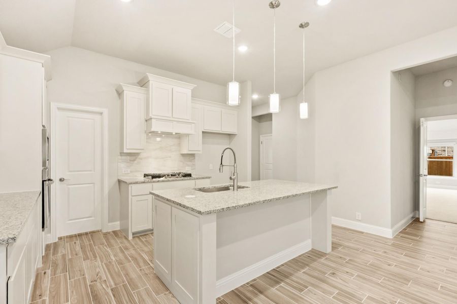 Kitchen with white cabinets, granite island with sink, pendant lights, and wood-look tile floors Kitchen with white cabinets, granite island with sink, pendant lights, and wood-look tile floors