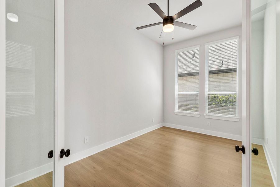 Bright office with wide-plank floors, dual windows, and sleek ceiling fan for airy comfort.