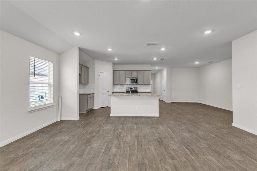 Open concept living area with wood-look flooring, recessed lighting, and white walls, featuring a kitchen with gray cabinetry, a kitchen island, and a stainless steel oven
