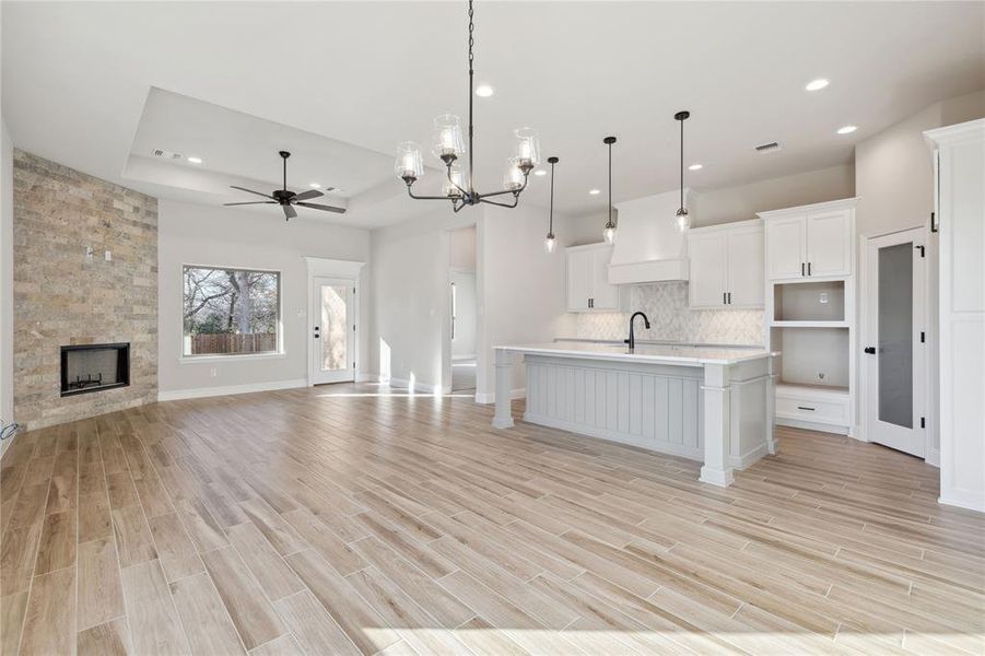 Kitchen with white cabinetry, hanging light fixtures, a tray ceiling, a center island with sink, and ceiling fan with notable chandelier