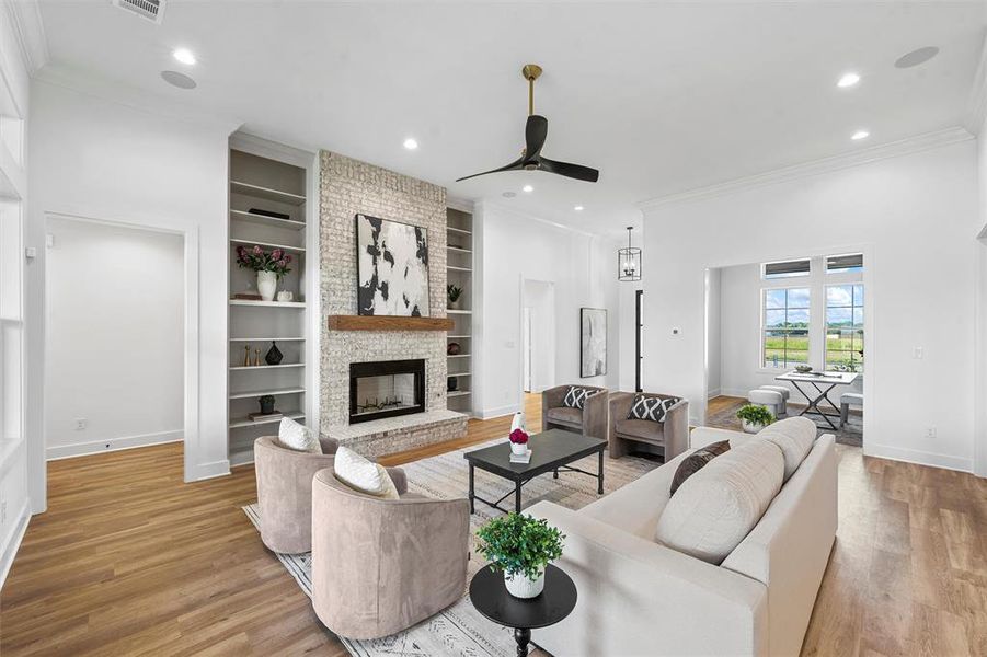 Living area with a ceiling fan, light wood-type flooring, ornamental molding, a brick fireplace, and built in shelves