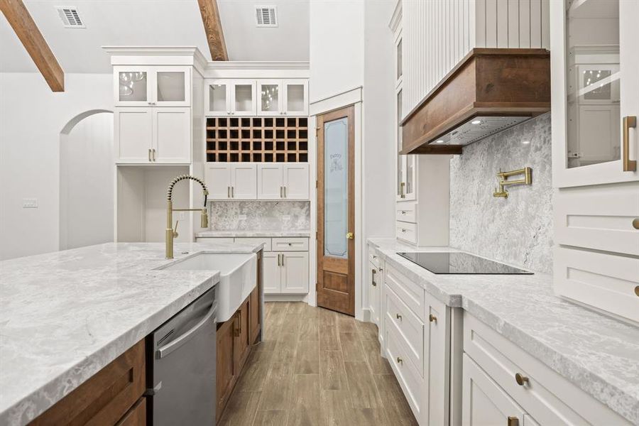 Spacious kitchen featuring an expansive island with a farmhouse sink, white perimeter cabinetry, and an integrated wine rack