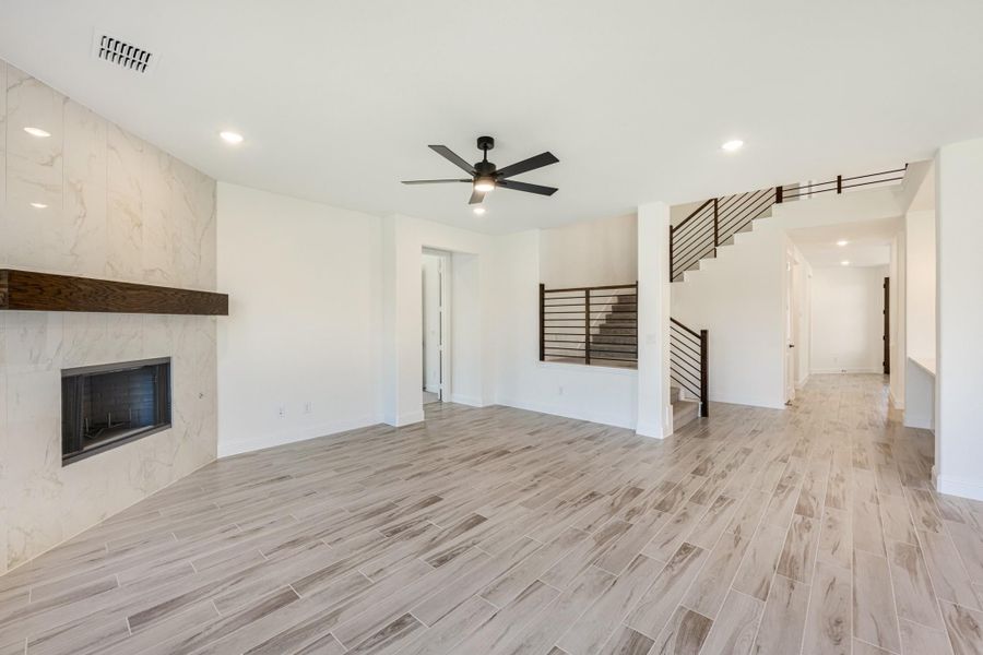 Open living room with marble tile fireplace, ceiling fan, wood-look floors, and staircase with metal railing Open living room with marble tile fireplace, ceiling fan, wood-look floors, and staircase with metal railing
