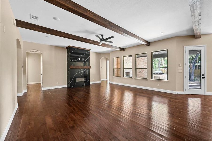 Unfurnished living room with beam ceiling, a fireplace, dark hardwood / wood-style flooring, and ceiling fan