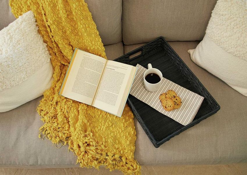 Staged living room with book, coffee cup, and yellow shawl on couch. Staged living room with book, coffee cup, and yellow shawl on couch.