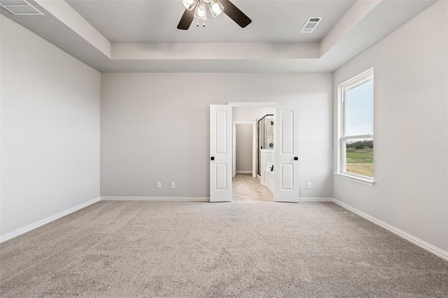 Unfurnished bedroom with a tray ceiling, a ceiling fan, and light carpet Unfurnished bedroom with a tray ceiling, a ceiling fan, and light carpet