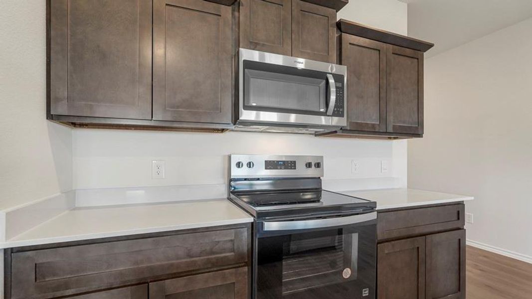 Kitchen featuring stainless steel appliances, dark wood-finish cabinetry, and white countertops