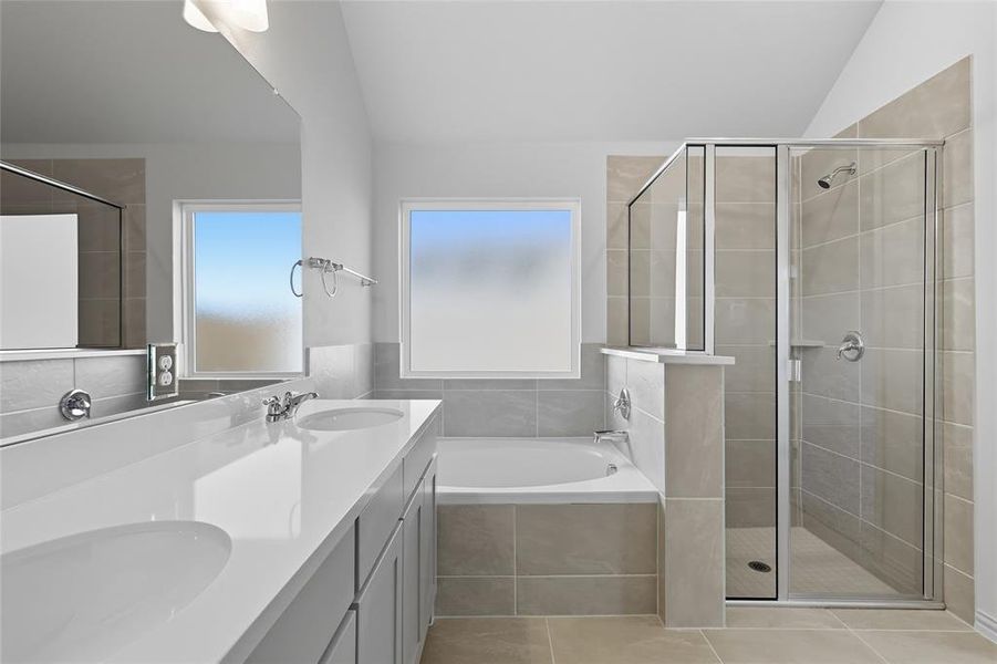 Full bath featuring a bath, double vanity, a stall shower, lofted ceiling, and light tile patterned floors Full bath featuring a bath, double vanity, a stall shower, lofted ceiling, and light tile patterned floors