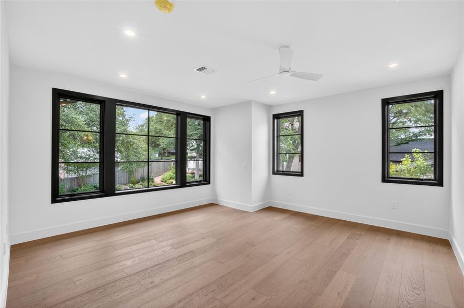 An airy bedroom with wide-plank hardwood floors and multiple windows that bring the outdoors in.