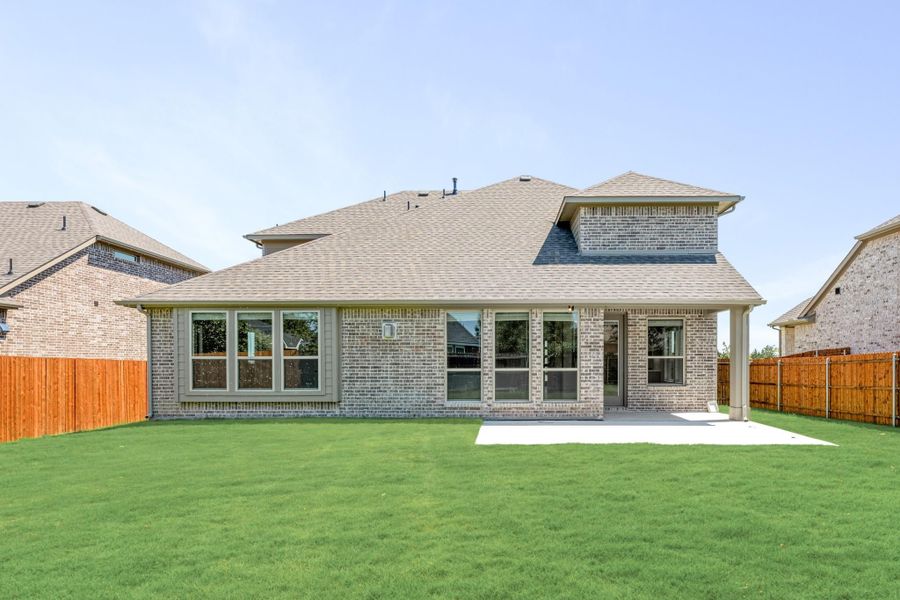 Rear view of brick home with covered patio, large windows, and fenced backyard with green lawn Rear view of brick home with covered patio, large windows, and fenced backyard with green lawn