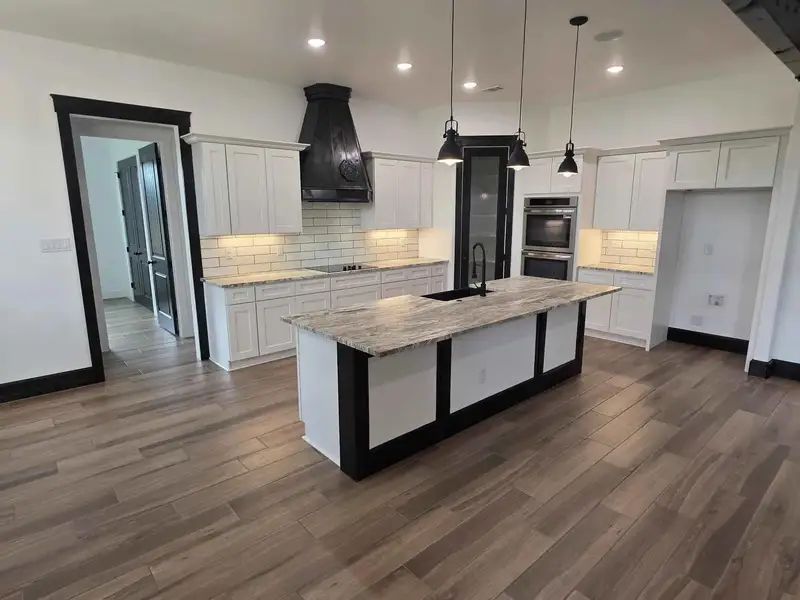 Kitchen featuring white cabinetry, a kitchen island with sink, light stone countertops, decorative backsplash, and hanging light fixtures Kitchen featuring white cabinetry, a kitchen island with sink, light stone countertops, decorative backsplash, and hanging light fixtures