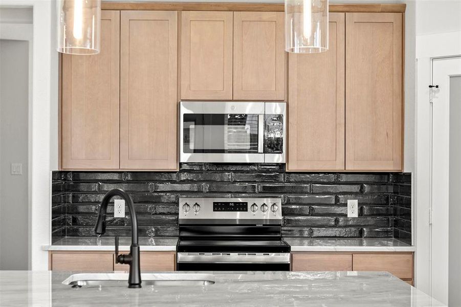 Kitchen featuring decorative backsplash, light brown cabinets, and appliances with stainless steel finishes