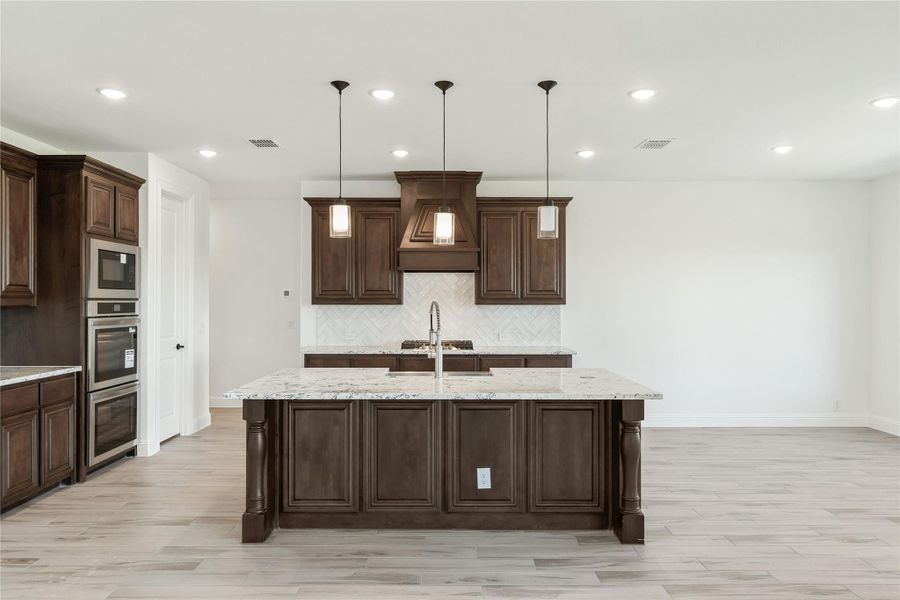 Kitchen with large granite island, dark wood cabinets, pendant lights, and stainless steel double ovens Kitchen with large granite island, dark wood cabinets, pendant lights, and stainless steel double ovens