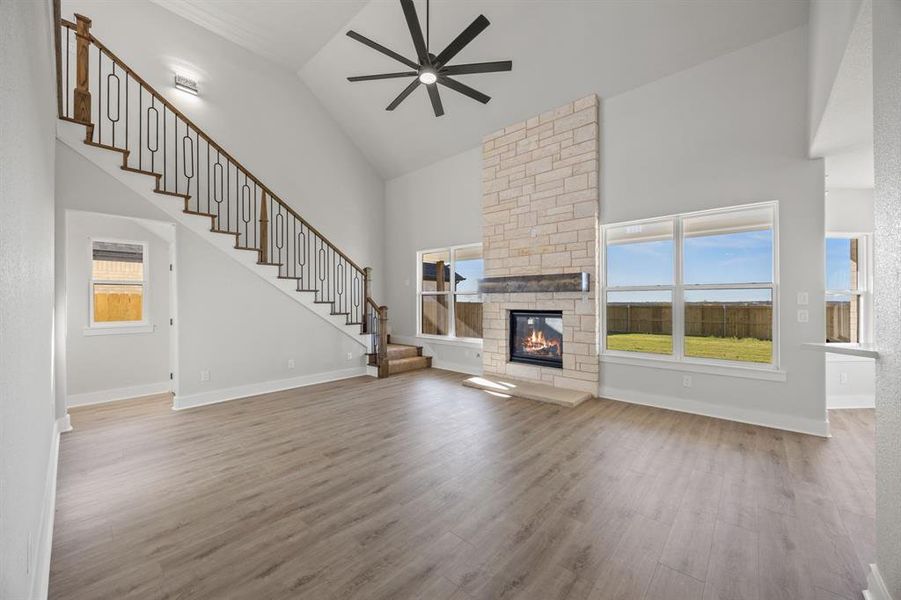 Unfurnished living room featuring high vaulted ceiling, stairway, light wood-type flooring, a stone fireplace, and ceiling fan
