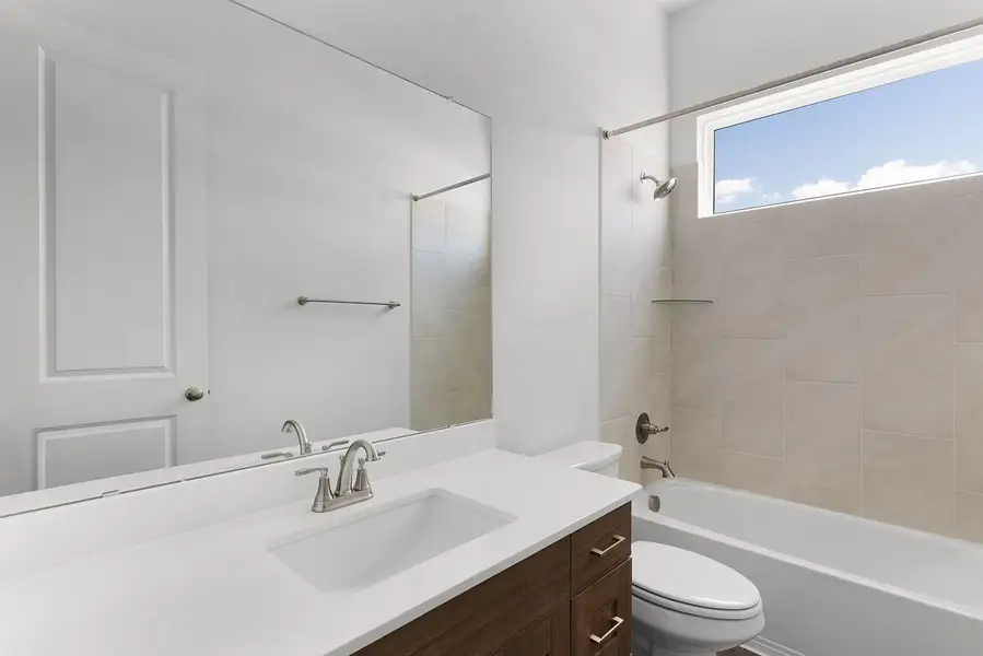 A well-appointed bathroom offers a clean vanity, bright mirror, and tub with an overhead window.
