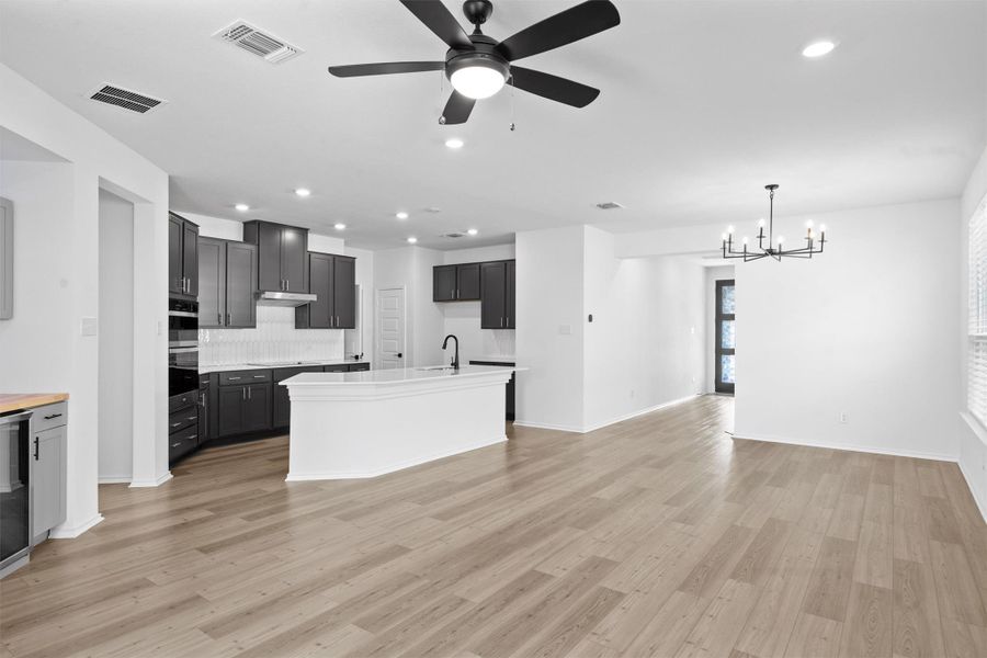 Kitchen with a ceiling fan, recessed lighting, backsplash, light wood-type flooring, and a kitchen island with sink