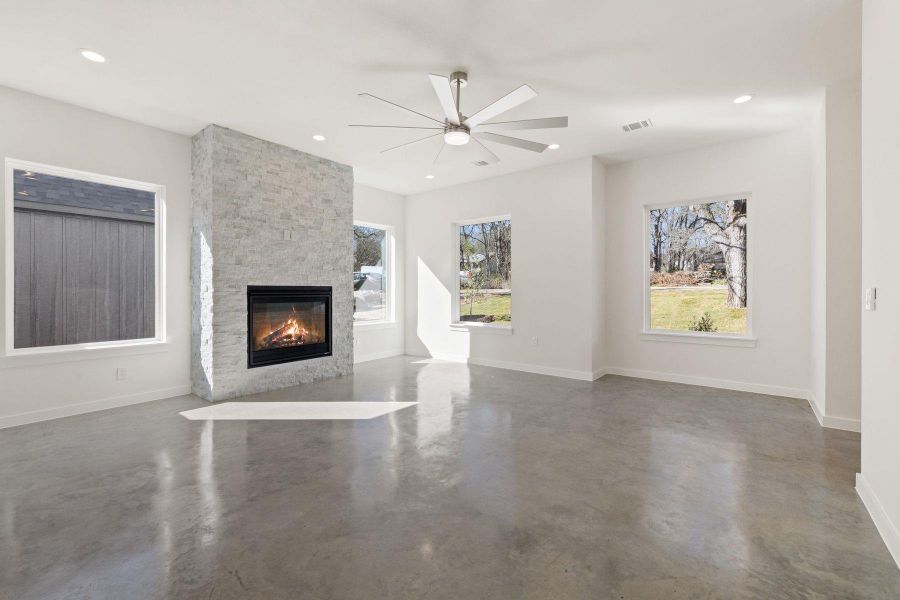 Unfurnished living room featuring recessed lighting, concrete floors, a stone fireplace, and baseboards