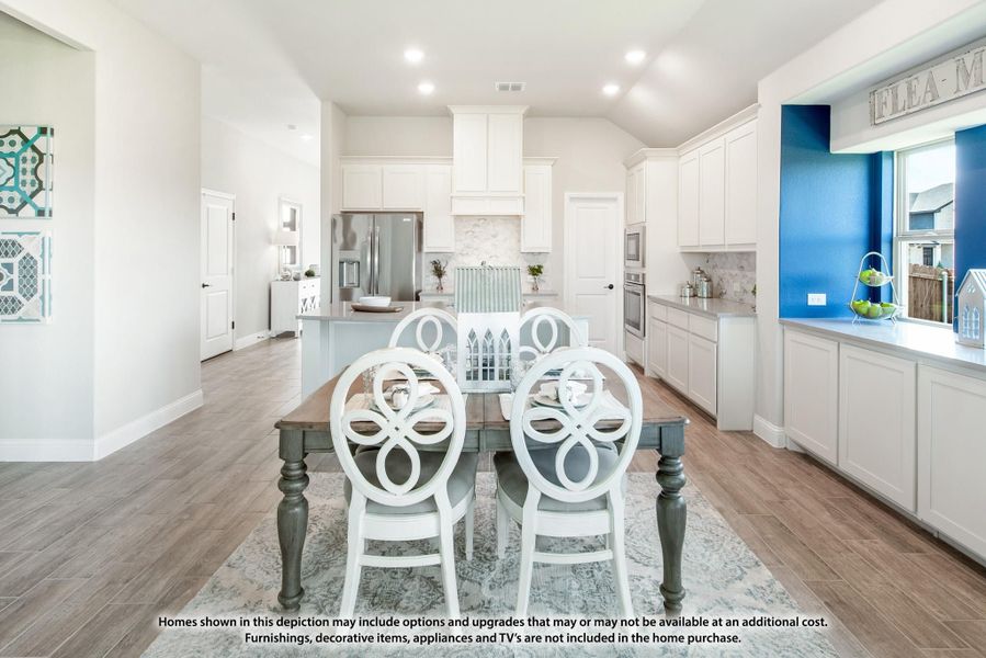 Open dining area with wood table and white chairs flowing into kitchen with white cabinets and blue accent wall