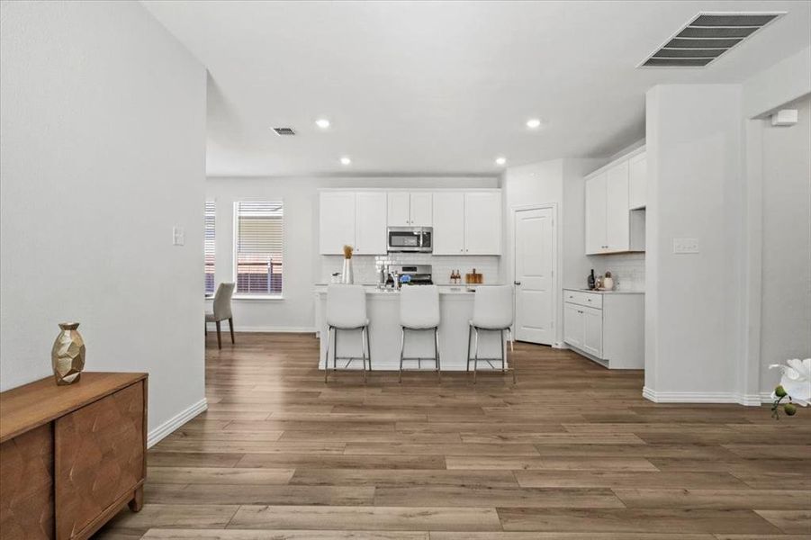Kitchen featuring a center island with sink, a kitchen bar, tasteful backsplash, white cabinets, and stainless steel microwave Kitchen featuring a center island with sink, a kitchen bar, tasteful backsplash, white cabinets, and stainless steel microwave