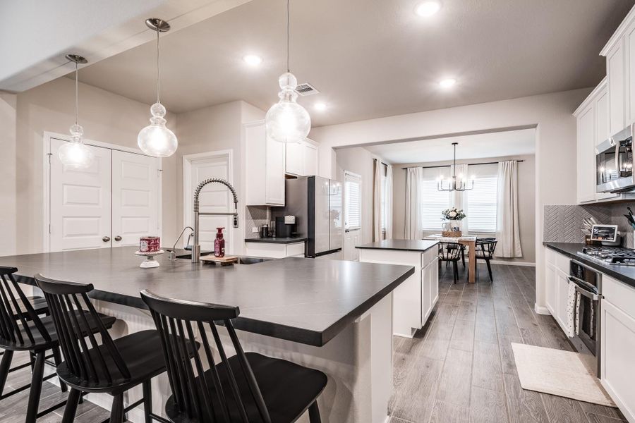 This modern kitchen features an open layout with sleek countertops, a large island with seating, pendant lighting, and stainless steel appliances. It flows into a bright dining area with large windows and contemporary decor. This modern kitchen features an open layout with sleek countertops, a large island with seating, pendant lighting, and stainless steel appliances. It flows into a bright dining area with large windows and contemporary decor.