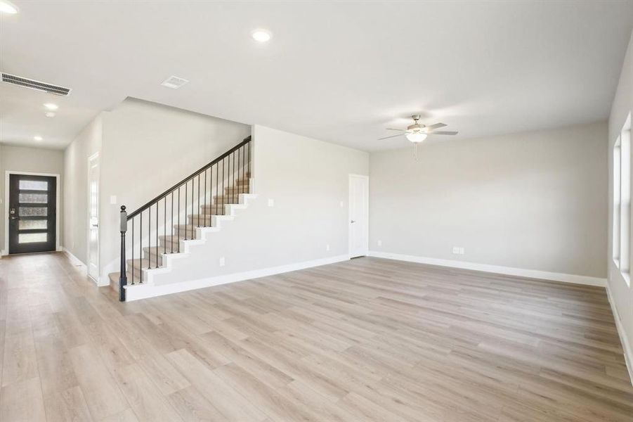 Unfurnished living room with light wood-style flooring, ceiling fan, recessed lighting, and stairs Unfurnished living room with light wood-style flooring, ceiling fan, recessed lighting, and stairs