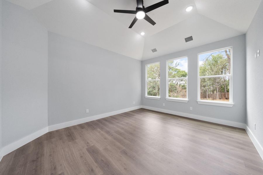 Spacious room featuring vaulted ceilings, wood-finish flooring, recessed lighting, a ceiling fan, and three large windows