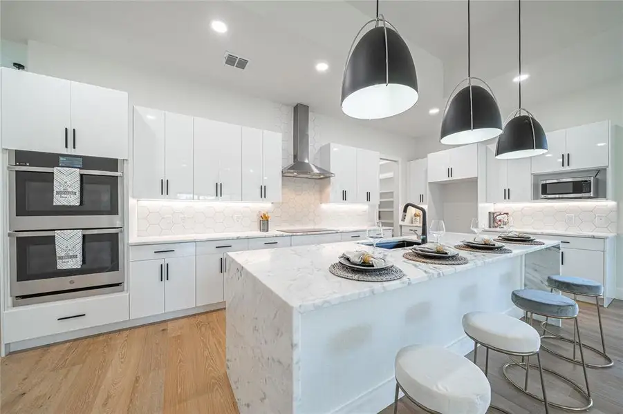 Kitchen featuring light stone counters, a kitchen breakfast bar, backsplash, light wood-style floors, and recessed lighting