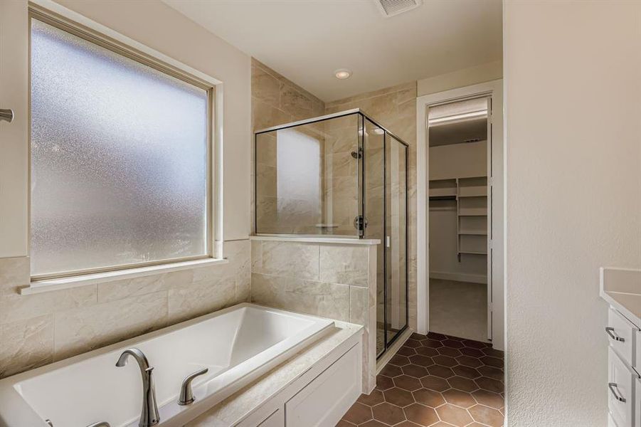 Full bath with a spacious closet, a bath, a shower stall, vanity, and dark tile patterned floors Full bath with a spacious closet, a bath, a shower stall, vanity, and dark tile patterned floors