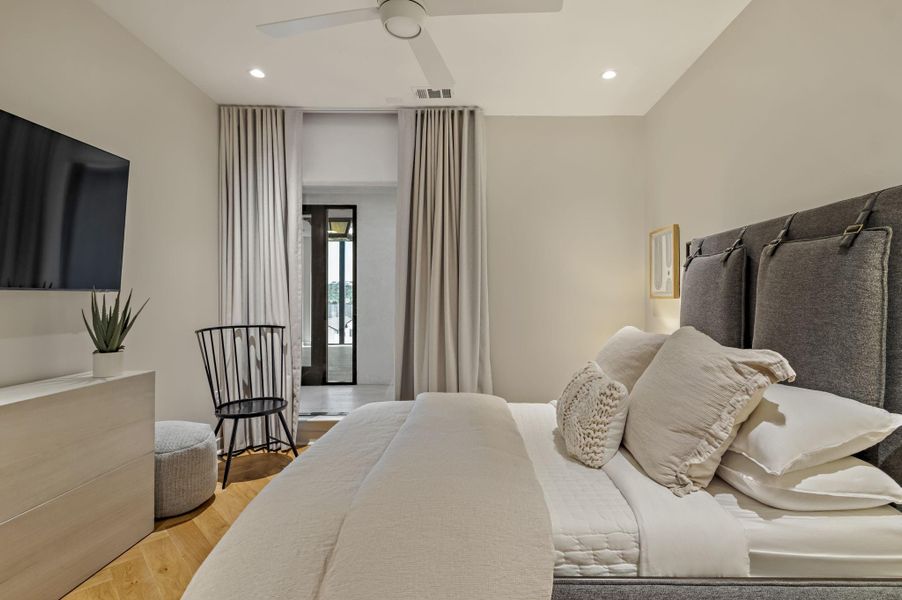 Herringbone hardwood floors complement this cozy bedroom with a ceiling fan and a view to the outdoors.
