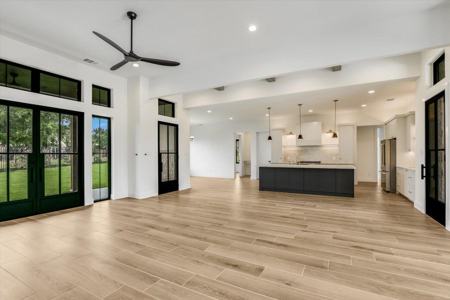Open-concept interior featuring wood-finish flooring, a modern kitchen with a dark-toned island, pendant lighting, and stainless steel appliances