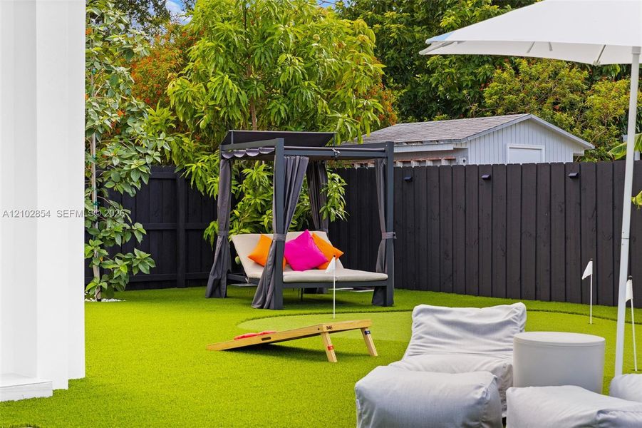 Backyard featuring synthetic turf, putting green with flags, and a dark-toned privacy fence