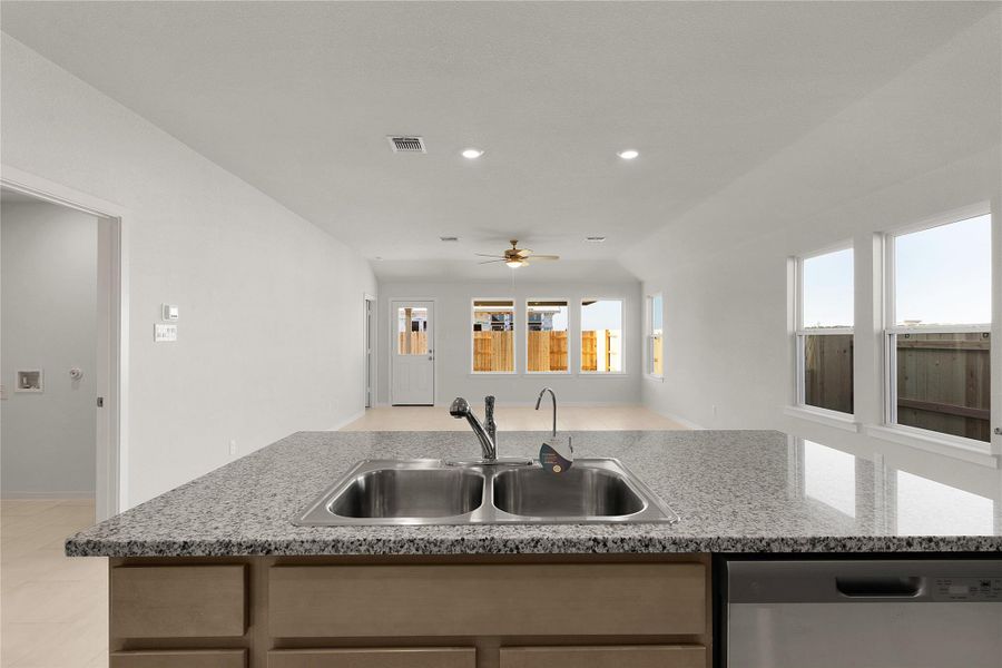 Kitchen featuring open floor plan, a ceiling fan, dishwasher, light wood finish cabinets, and a kitchen island with sink
