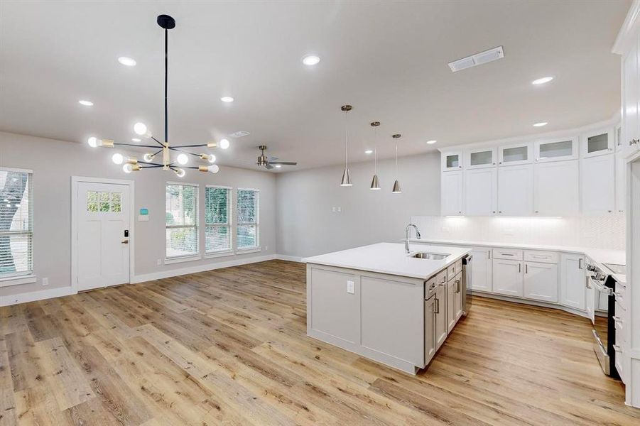 Kitchen featuring white cabinets, ceiling fan with notable chandelier, sink, hanging light fixtures, and an island with sink