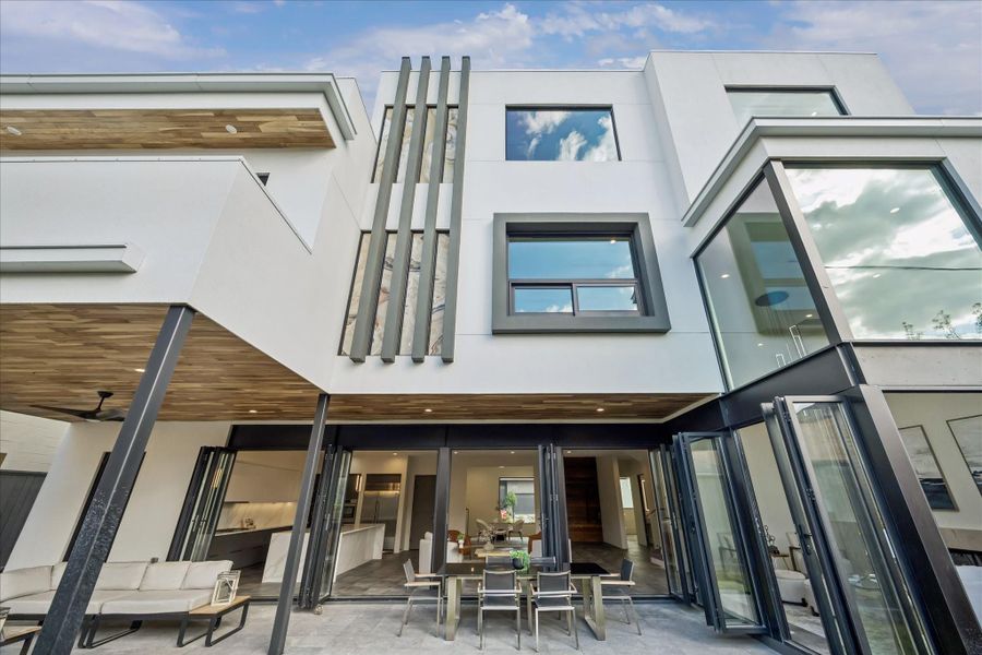 This modern home features an open facade with large windows and sliding glass doors, offering seamless indoor-outdoor living. The contemporary design includes a spacious patio area, perfect for entertaining.