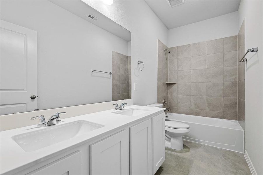 Full bathroom with tile patterned flooring, double sink vanity, toilet, and tiled shower / bath