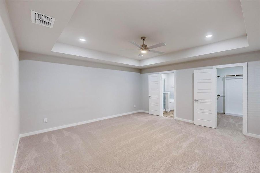 Unfurnished bedroom with ceiling fan, a raised ceiling, a spacious closet, and connected bathroom