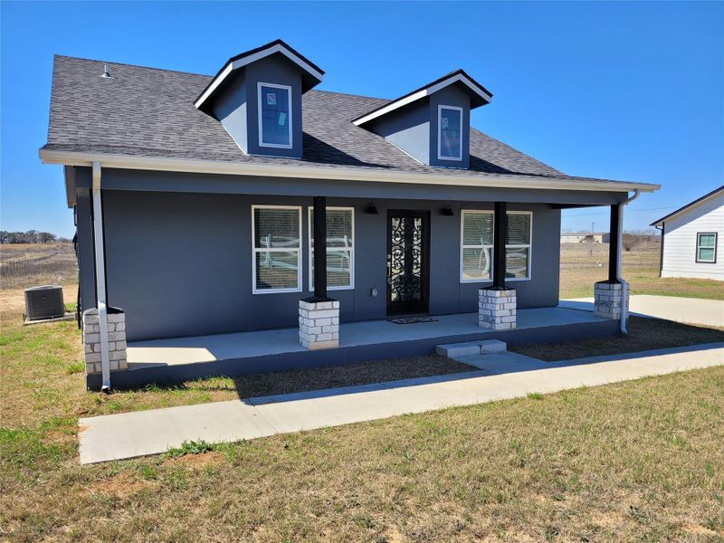 View of front of house with covered porch, a front yard, and roof with shingles