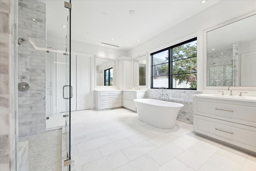 [Primary Bath]The sumptuous primary bath offers resort-inspired luxury with gleaming marble countertops and floors; separate sink cabinets; a vanity; two water closets; a frameless glass and marble shower; and a free-standing tub.