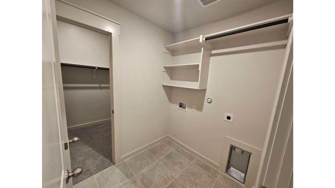 Utility area featuring tile flooring, built-in shelving, a clothes hanging rod, washer/dryer hookups, and a nearby closet with carpeted flooring and a hanging rod