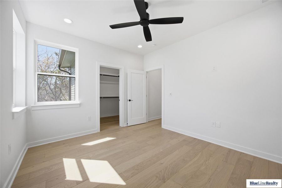 Unfurnished bedroom featuring a spacious closet, light wood finished floors, ceiling fan, and recessed lighting
