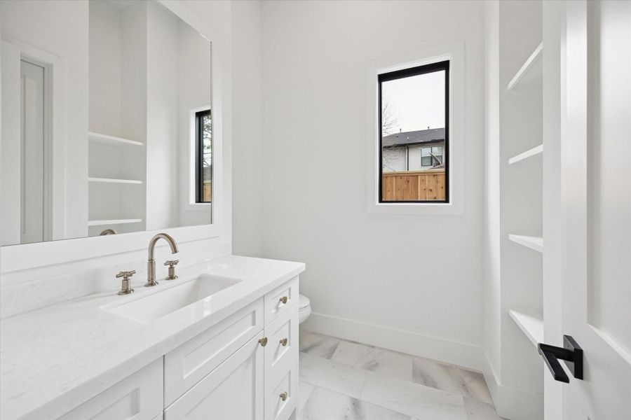 Bright and airy half bath featuring quartz countertops, a custom shaker vanity, and polished nickel fixtures for a timeless finish. Open shelving and a sleek black framed window add modern contrast and thoughtful design detail.