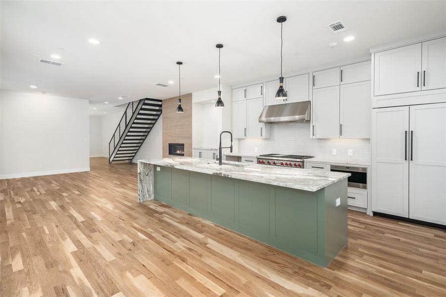 Kitchen with hanging light fixtures, white cabinetry, sink, and light stone countertops