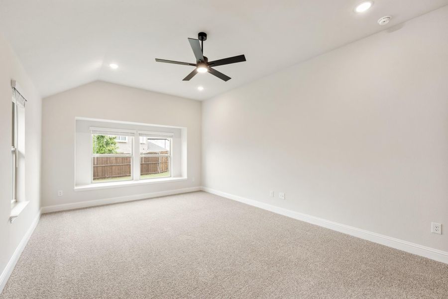 Empty bedroom with vaulted ceiling, ceiling fan, carpet flooring, and large window with backyard view Empty bedroom with vaulted ceiling, ceiling fan, carpet flooring, and large window with backyard view