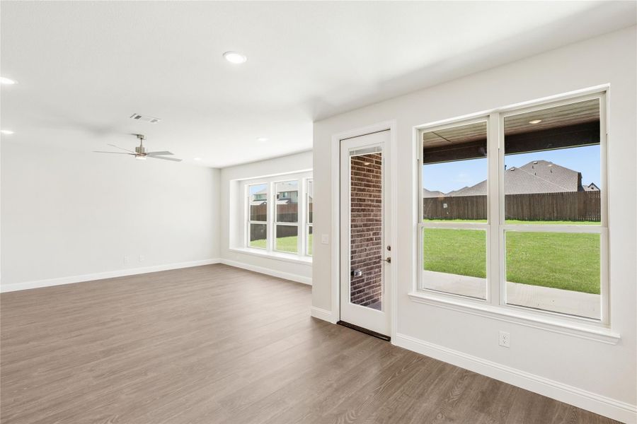 Open living area with wood-look floors, ceiling fan, and back door with large windows overlooking fenced yard