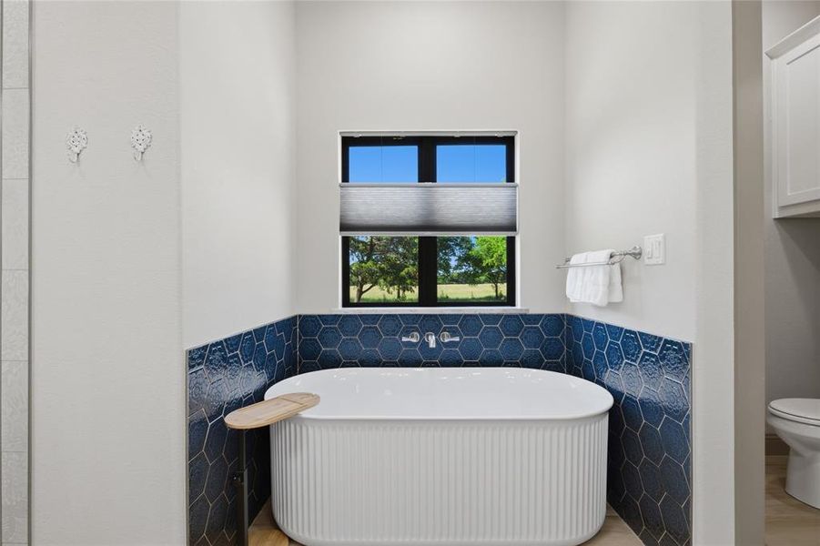 Freestanding soaking tub featuring a fluted base and a wall-mounted faucet, set against a hexagonal blue tile wainscoting