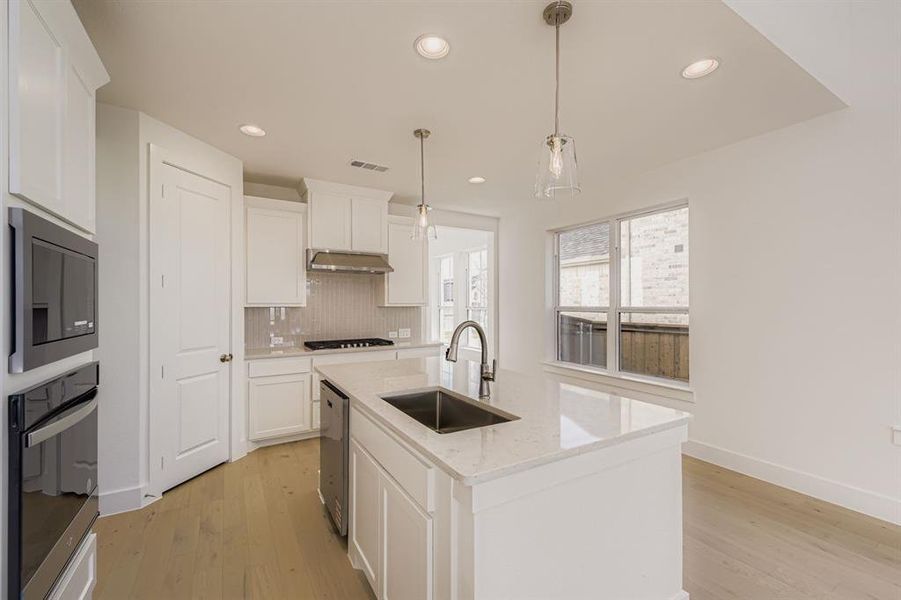 Kitchen featuring a kitchen island with sink, backsplash, light wood-style floors, appliances with stainless steel finishes, and recessed lighting