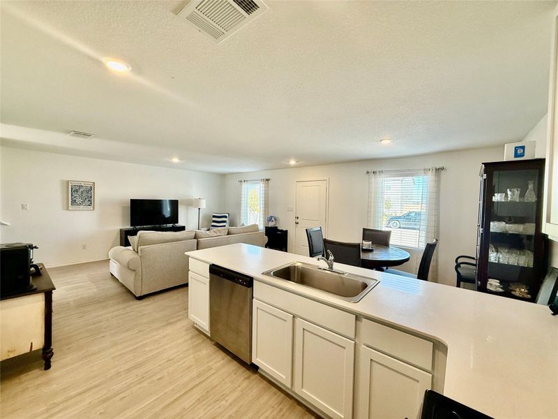 Kitchen with light countertops, a textured ceiling, stainless steel dishwasher, white cabinets, and open floor plan