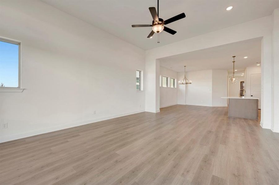 Unfurnished living room featuring ceiling fan, light wood-type flooring, and hanging lights Unfurnished living room featuring ceiling fan, light wood-type flooring, and hanging lights
