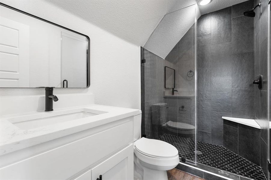 Bathroom featuring toilet, a shower with shower door, vaulted ceiling, a textured ceiling, and vanity