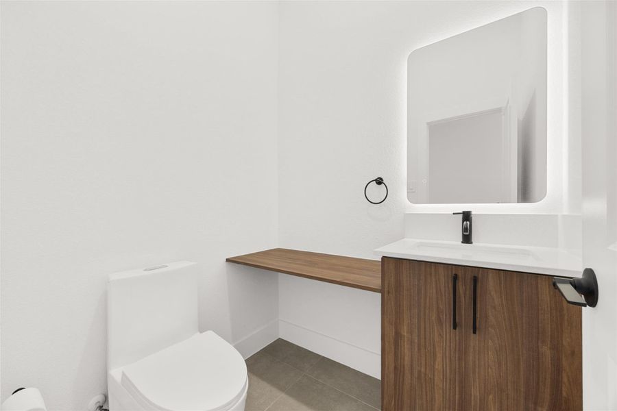 Half bath with custom designed vanity, quartz countertop, and backlit mirror.